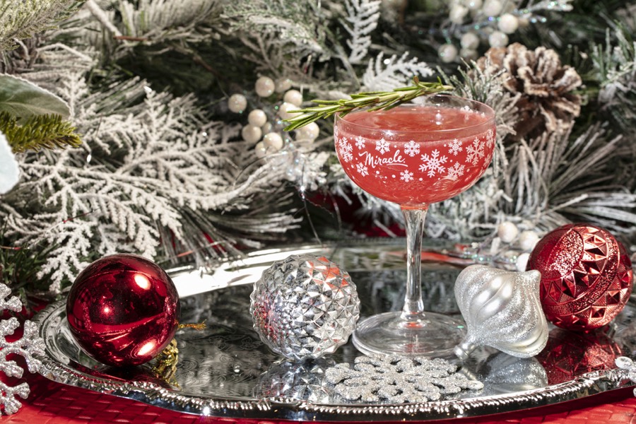 A pink cocktail in a snowflake-printed Miracle coupe, garnished with rosemary.