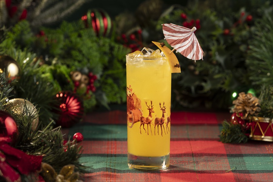 A tall glass printed with Santa&rsquo;s sleigh and reindeer, filled with a golden drink and topped with a candy-stripe umbrella.