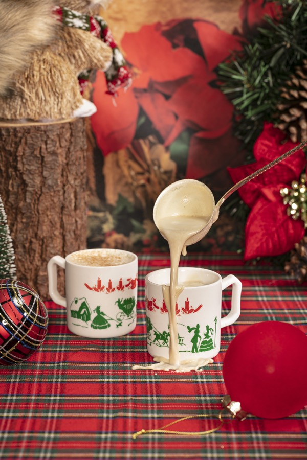 Nog being ladled into a vintage Miracle mug printed in red and green, on a tartan cloth.