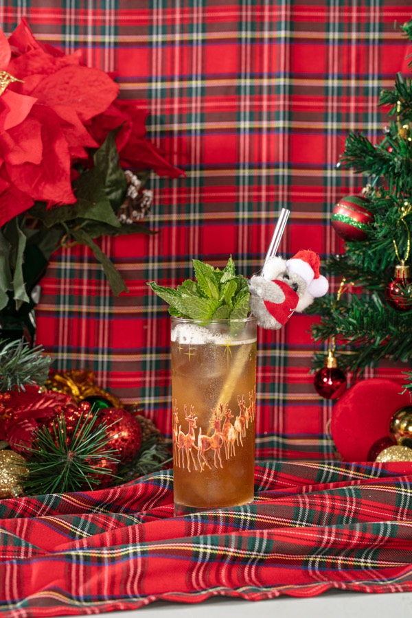A tall reindeer-printed glass with a bouquet of mint and a small plush koala clipped to the straw.
