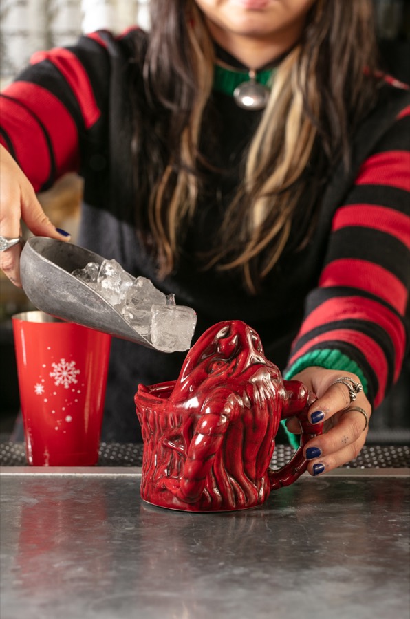 A bartender scooping cracked ice into the red ceramic Krampus mug at the bar.