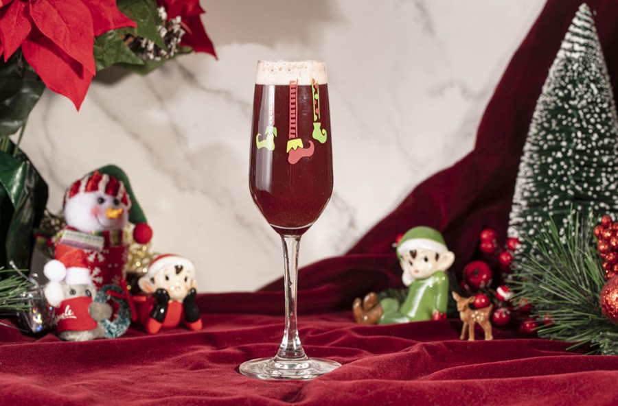 A deep red sparkling drink in a flute printed with elf legs and a ladder.