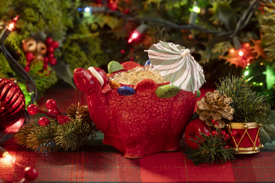 A red ceramic stegosaurus mug filled with crushed ice and topped with a green paper umbrella.