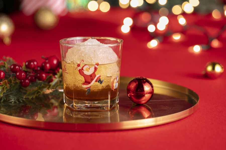 An amber cocktail in a dancing-Santa rocks glass, packed with a dome of crushed ice.