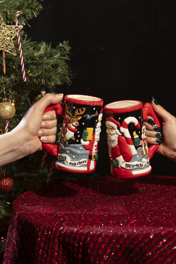 Guests in Santa hats raising Miracle steins beside a decorated tree.