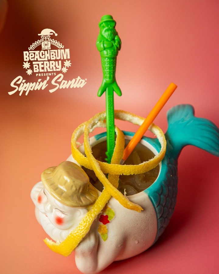 A Santa-mermaid mug with a turquoise tail, a lemon peel coil and a green Sippin&rsquo; Santa swizzle stick.